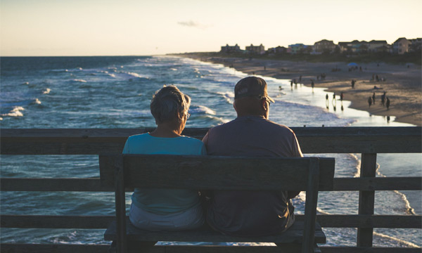 Couple sitting on bench looking at ocean shore